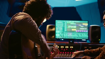 Young artist songwriter composing a new song on guitar in recording session at studio, creating...