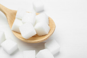 Many sugar cubes and wooden spoon on white table, closeup. Space for text
