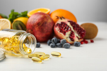Vitamin pills, bottle and fresh fruits on white wooden table. Space for text