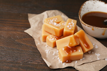 Delicious candies with sea salt and caramel sauce on wooden table, closeup. Space for text