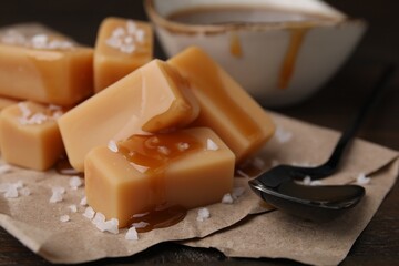 Delicious candies with sea salt and caramel sauce on wooden table, closeup
