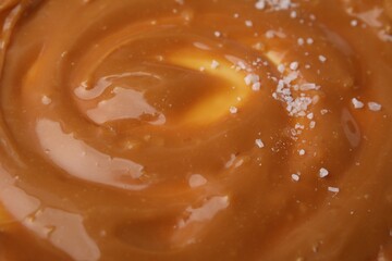 Delicious caramel sauce with sea salt as background, closeup