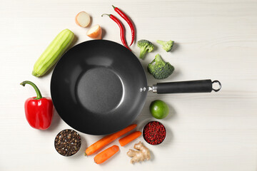Empty iron wok surrounded by raw ingredients on white wooden table, flat lay
