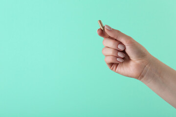 Woman holding vitamin capsule on turquoise background, closeup with space for text. Health...