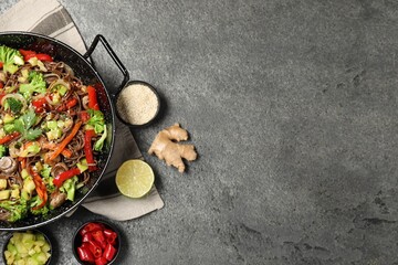 Wok with noodles, mushrooms, vegetables and other products on grey table, flat lay. Space for text
