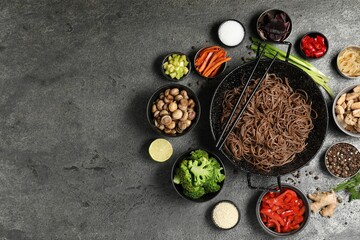 Wok with noodles, chicken and other products on grey table, flat lay. Space for text