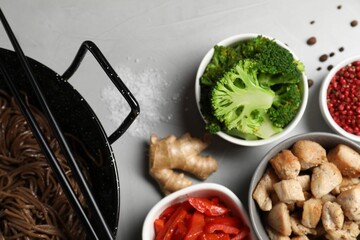 Wok with noodles, chicken and other products on light grey table, flat lay