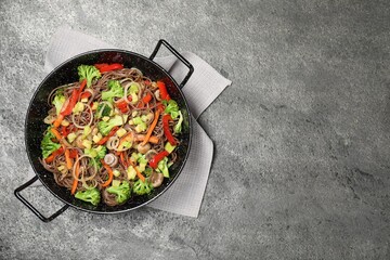 Stir fried noodles with mushrooms and vegetables in wok on grey table, top view. Space for text