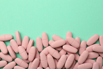 Pink vitamin capsules on turquoise background, top view. Space for text