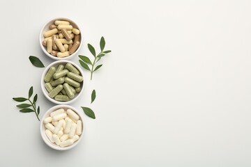 Different vitamin capsules in bowls and leaves on white background, flat lay. Space for text
