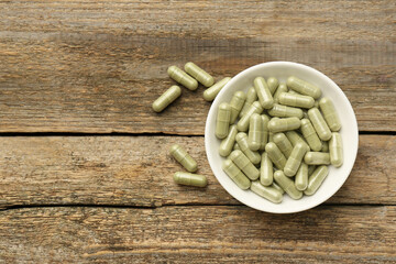 Vitamin capsules in bowl on wooden table, top view. Space for text