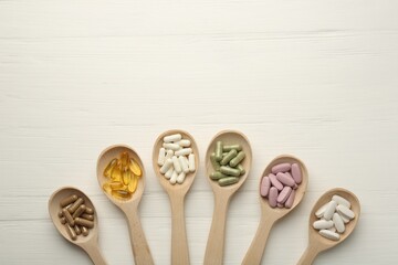 Different vitamin capsules in spoons on white wooden table, flat lay. Space for text