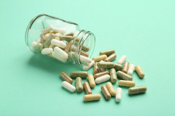 Vitamin pills and bottle on mint color background, closeup