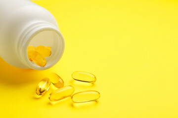 Softgel capsules and bottle on yellow background, closeup. Space for text