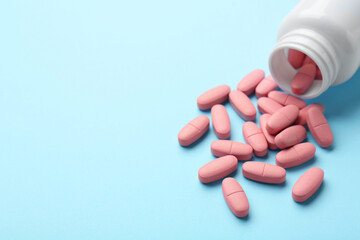 Vitamin pills and bottle on light blue background, closeup. Space for text