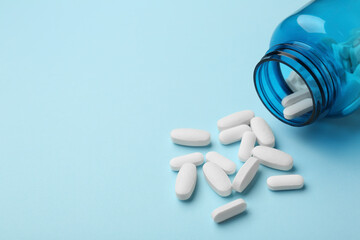 Vitamin pills and bottle on light blue background, closeup. Space for text