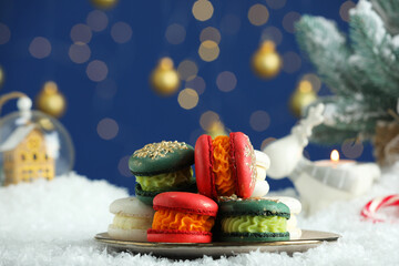 Different decorated Christmas macarons on table with artificial snow against blurred lights
