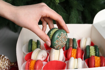 Woman with box of decorated Christmas macarons at table, closeup