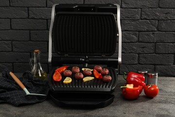 Electric grill with meat balls, bell peppers and lemon on grey textured table