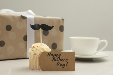 Card with phrase Happy Father's Day and delicious cupcake with mustache topper on light table