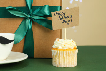 Happy Father's Day. Tasty cupcake with greetings and gift box on green table, closeup