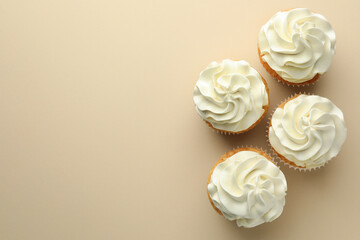 Tasty vanilla cupcakes with cream on beige background, top view. Space for text