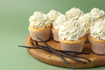Tasty cupcakes with cream and vanilla pods on green background