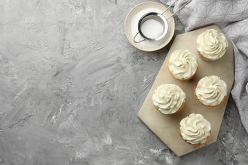 Tasty cupcakes with vanilla cream on grey table, top view. Space for text