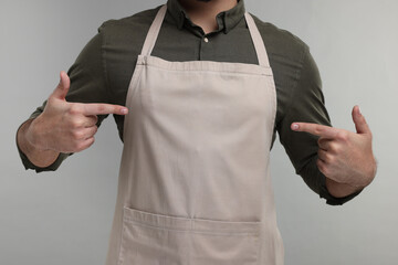 Man pointing at kitchen apron on grey background, closeup. Mockup for design