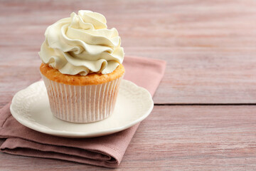 Tasty cupcake with vanilla cream on pink wooden table, closeup. Space for text