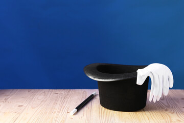 Magician's hat, wand and gloves on wooden table against blue background, space for text