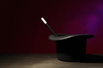 Magician's hat and wand on black wooden table against dark background, space for text