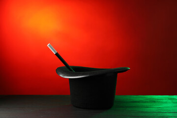 Magician's hat and wand on black wooden table against color background