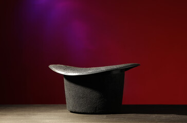 Magician's hat on black wooden table against color background