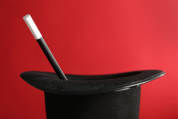 Black magician's hat and wand on red background, closeup