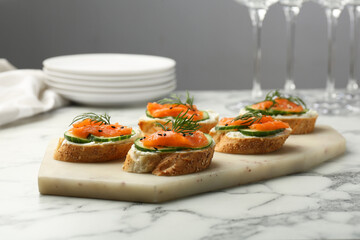 Tasty canapes with salmon, cucumber and cream cheese on white marble table