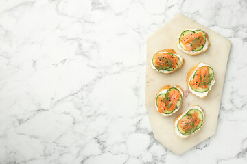 Tasty canapes with salmon, cucumber and cream cheese on white marble table, top view. Space for text