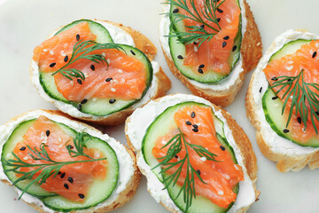 Tasty canapes with salmon, cucumber and cream cheese on board, top view