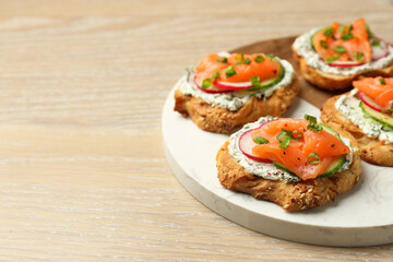 Tasty canapes with salmon, cucumber, radish and cream cheese on wooden table, space for text