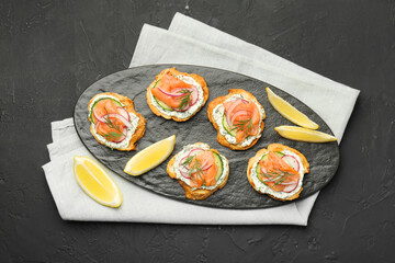 Tasty canapes with salmon, cucumber, radish and cream cheese on black table, top view