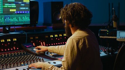 Music producer editing tracks with mixing console and audio software in studio, pressing key...
