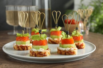 Tasty canapes with salmon, cucumber, bread and cream cheese on wooden table, closeup