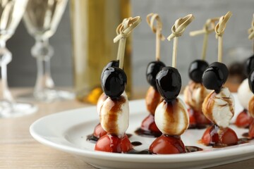 Tasty canapes with black olives, mozzarella and cherry tomatoes on light wooden table, closeup