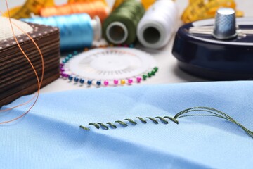 Light blue cloth with sewing thread and stitches on table, closeup