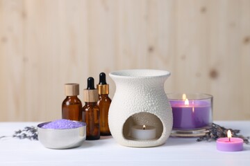 Different aromatherapy products and burning candles on white wooden table