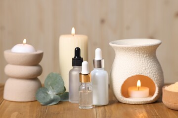 Different aromatherapy products, burning candles and eucalyptus leaves on wooden table
