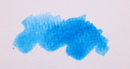 Blot of blue watercolor paint on white paper, top view