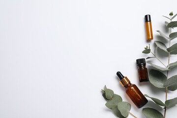 Aromatherapy. Bottles of essential oil and eucalyptus branches on white background, flat lay. Space...