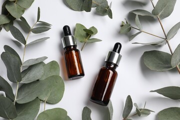 Aromatherapy. Bottles of essential oil and eucalyptus leaves on white background, flat lay
