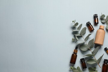 Aromatherapy. Bottles of essential oil and eucalyptus leaves on light grey background, flat lay....